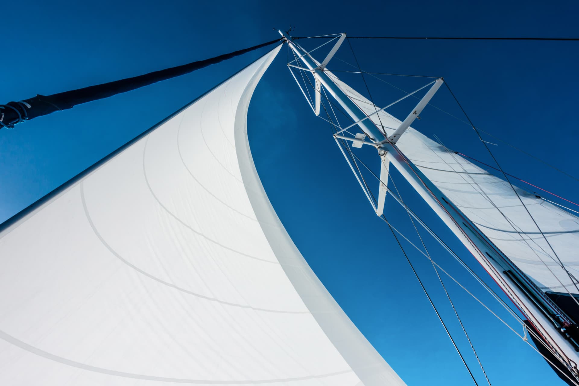 Mainsail and mast seen from below against a clear blue sky